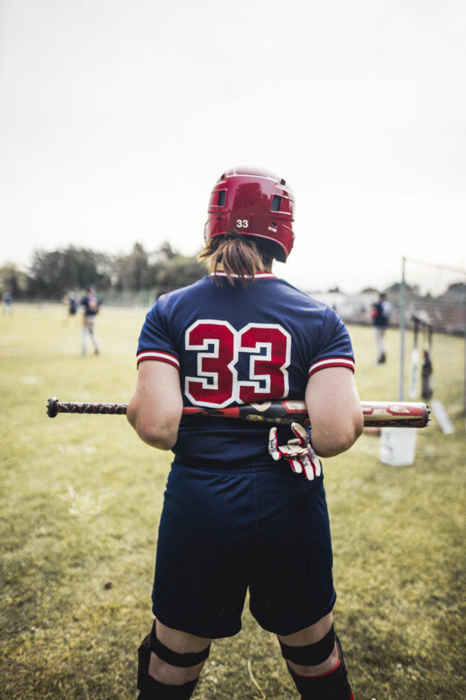 Frau mit Trikotnummer 33 von hinten mit Blick aufs Spielfeld. Sie hält ihren Schläger hinter ihrem Rücken verschränkt.
