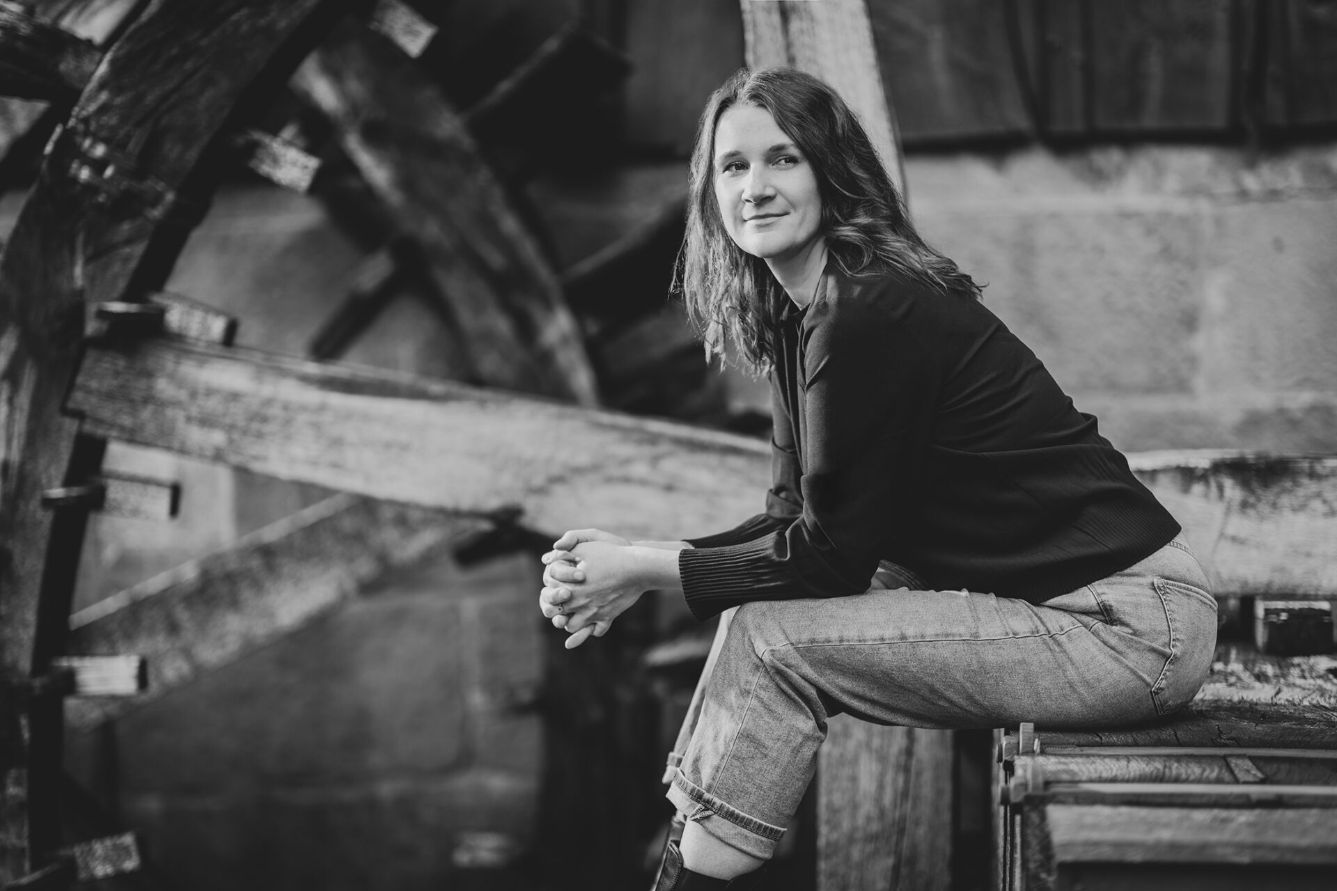 Fotografin Yvonne Koall leichtt vornüberbeugt mit verschränkten Händen in einer alten Mühle sitzend