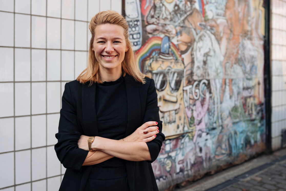 Britta Cornelißen, Blonde Frau in schwarzem Blazer mit überkreuzten Armen vor Graffiti Wand