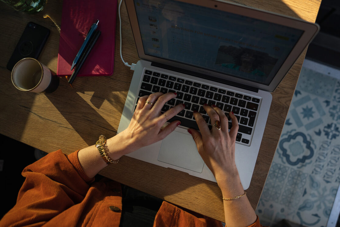 von der Sonne angeleuchtete Hände am Laptop tippend am Schreibtisch. Aus der Vogelperspektive