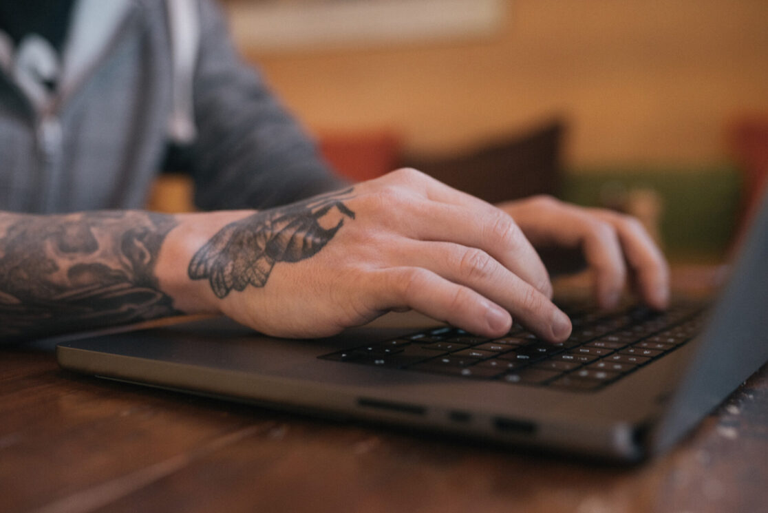 Tätowierte Hände schreiben an einem Laptop