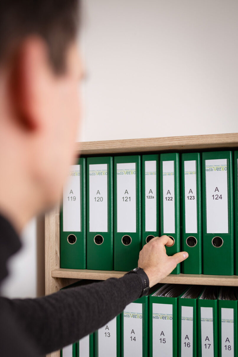 Mann nimmt einen Aktenordner aus dem Regal